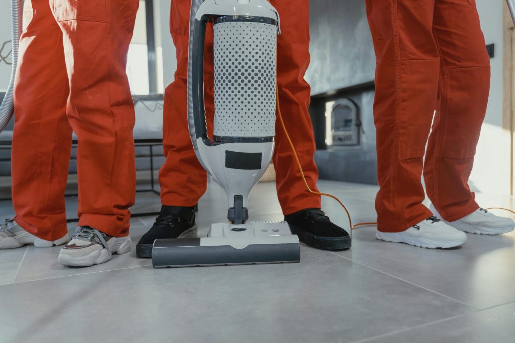 Une équipe de nettoyeurs professionnels en uniformes rouges utilisant un aspirateur à l'intérieur.